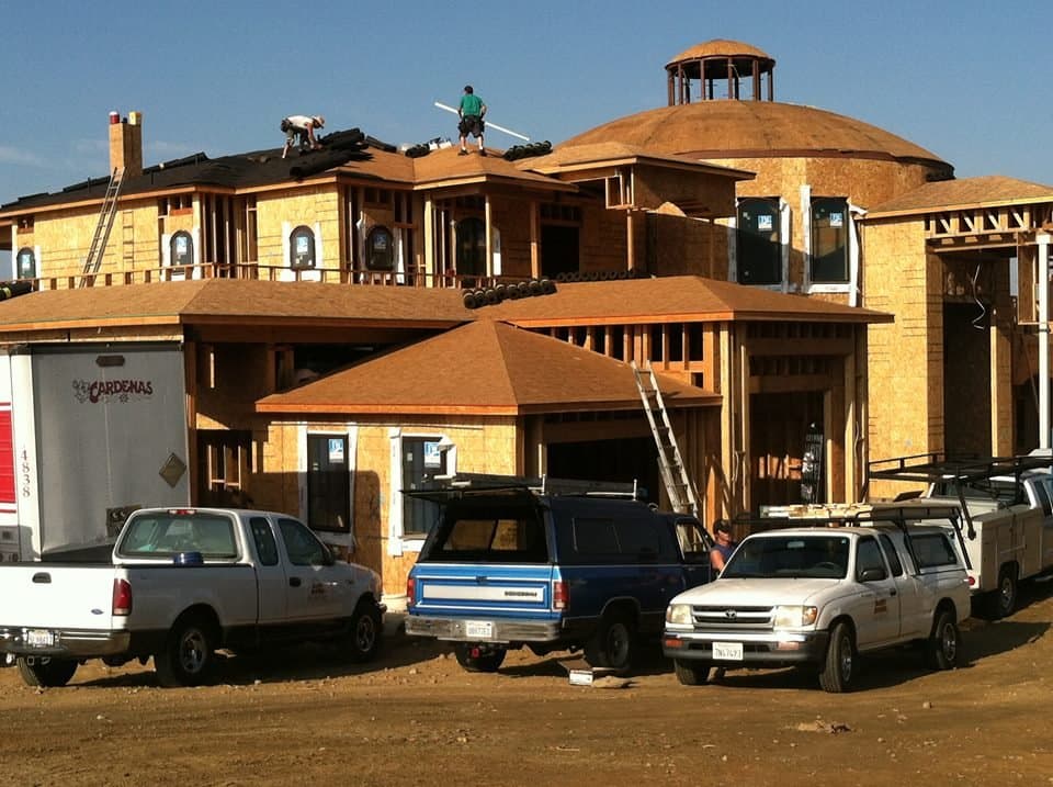Baker Roofing trucks at a large custom home under construction with the crew roofing the second story